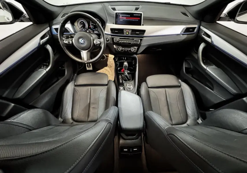 Vue intérieure avant de la BMW X2 xDrive25e M Sport 2022, sièges cuir noirs et tableau de bord avec écran central.