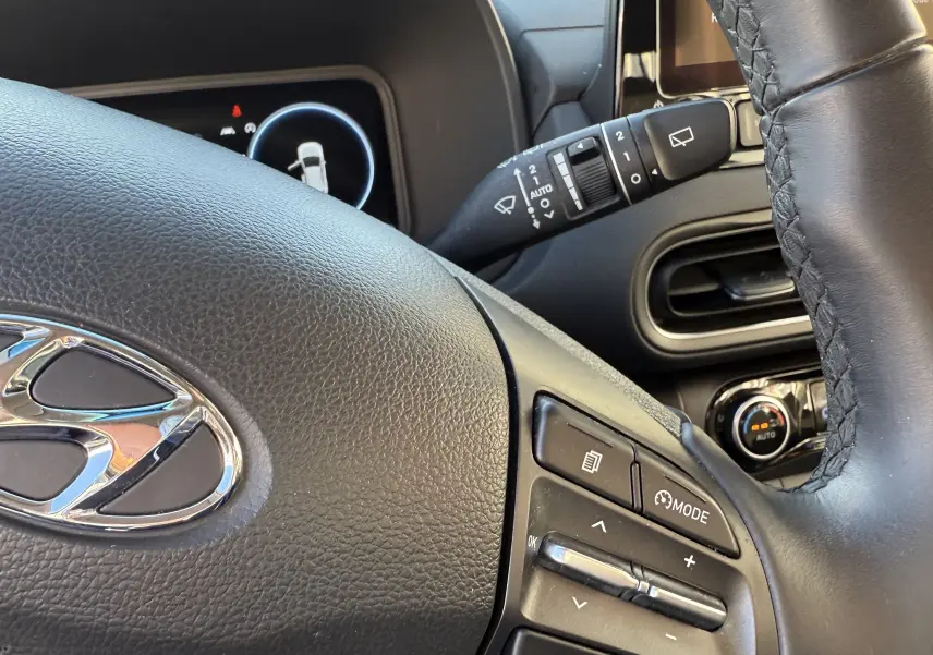 Gros plan sur le volant noir du Hyundai Kona blanc Atlas 2021, avec commandes multifonctions et tableau de bord partiel.