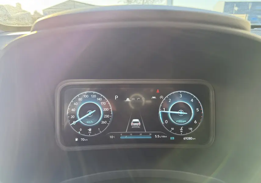 Vue rapprochée du tableau de bord numérique du Hyundai Kona blanc, affichant vitesse, régime moteur et indicateurs de conduite.