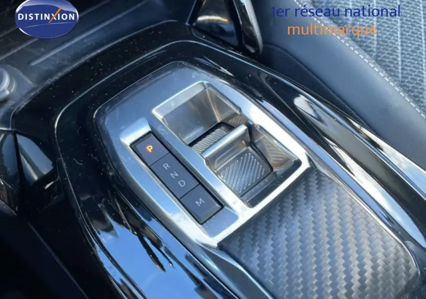 Gros plan sur la console centrale noire de la Peugeot 208 hybride 2025 avec sélecteur de boîte automatique et finition carbone.