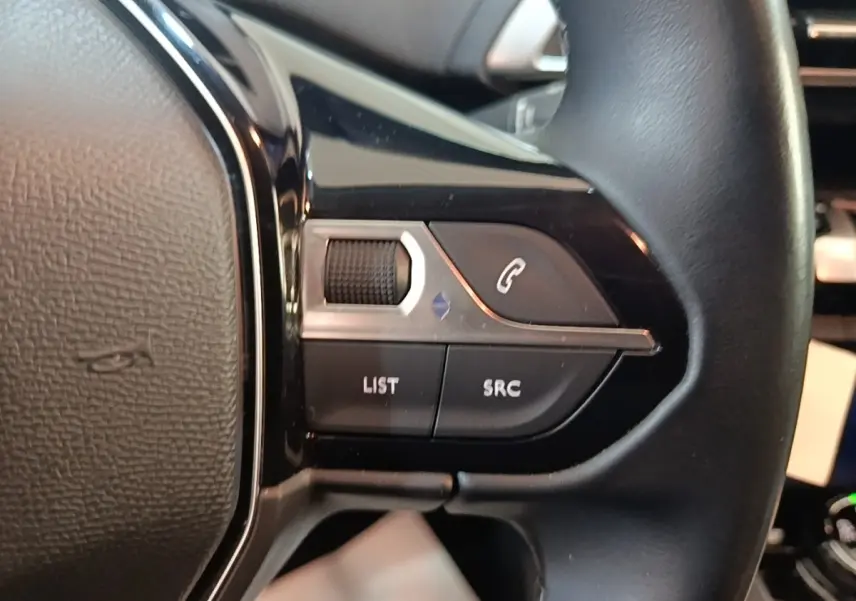 Gros plan sur les commandes gauche du volant cuir noir du Peugeot 5008, boutons pour téléphone et audio visibles.