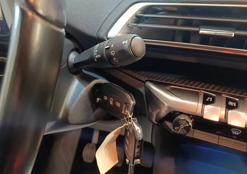 Gros plan intérieur sur le volant et la clé de contact du Peugeot 5008 noir, avec commandes et tableau de bord partiellement visibles.