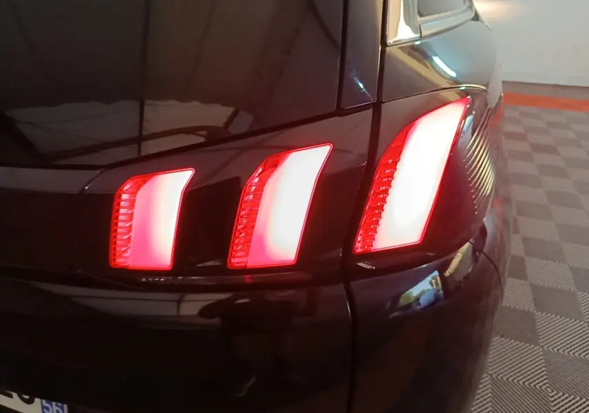 Gros plan sur le feu arrière droit rouge allumé d’un Peugeot 5008 noir, avec reflet sur la carrosserie brillante.