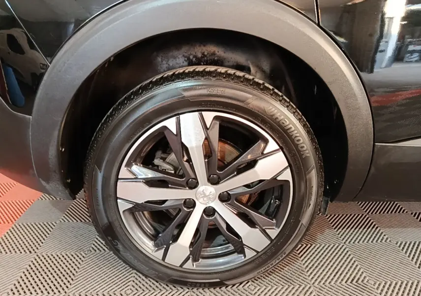 Gros plan sur la roue avant droite noire du Peugeot 5008 2018 avec jante alliage bicolore et logo lion central.