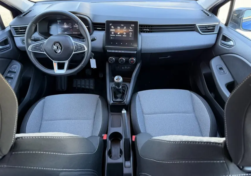 Vue intérieure avant de la Renault Clio Evolution TCe 90 2024, tableau de bord avec écran tactile central et sièges gris.