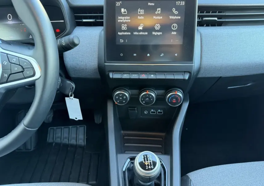 Vue intérieure centrée sur la console centrale et volant de la Renault Clio bleu, avec levier de vitesses manuel et écran tactile.