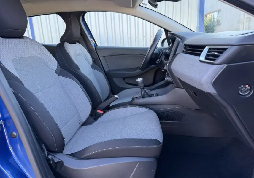 Vue intérieure côté conducteur de la Renault Clio Evolution TCe 90 2024, sièges tissu gris et noir, volant cuir et tableau de bord moderne.