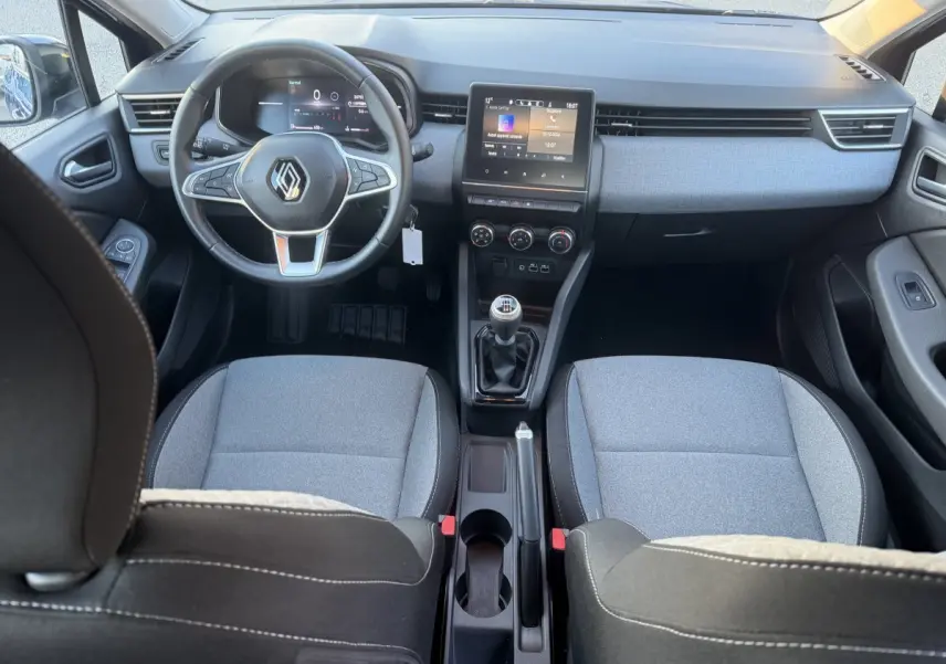 Vue intérieure avant de la Renault Clio Evolution TCe 90 2024, sièges gris, volant cuir multifonctions et écran tactile central.