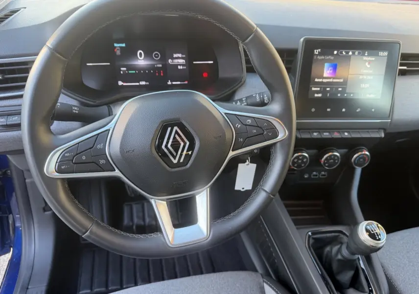 Vue intérieure centrée sur le volant cuir et le tableau de bord digital de la Renault Clio bleu 2024 avec écran tactile et boîte manuelle.