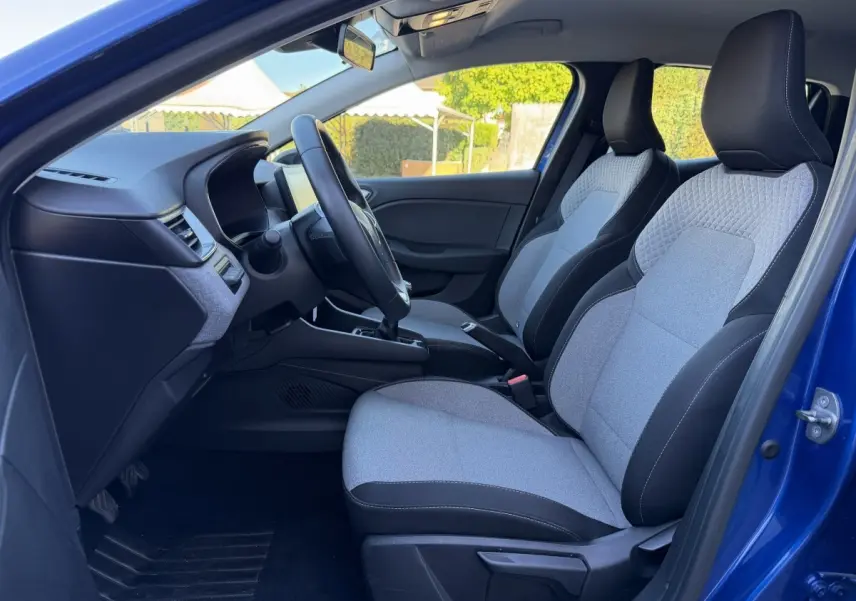 Vue intérieure côté conducteur de la Renault Clio Evolution TCe 90 2024 bleu, sièges tissu gris et noir, volant multifonctions.
