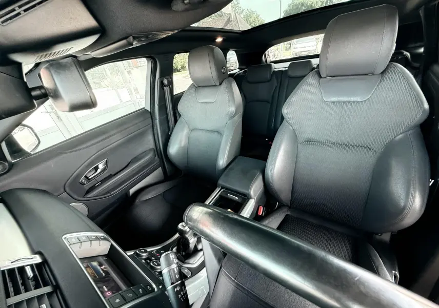 Intérieur noir du Range Rover Evoque vu côté conducteur, mettant en valeur les sièges avant et le toit panoramique.