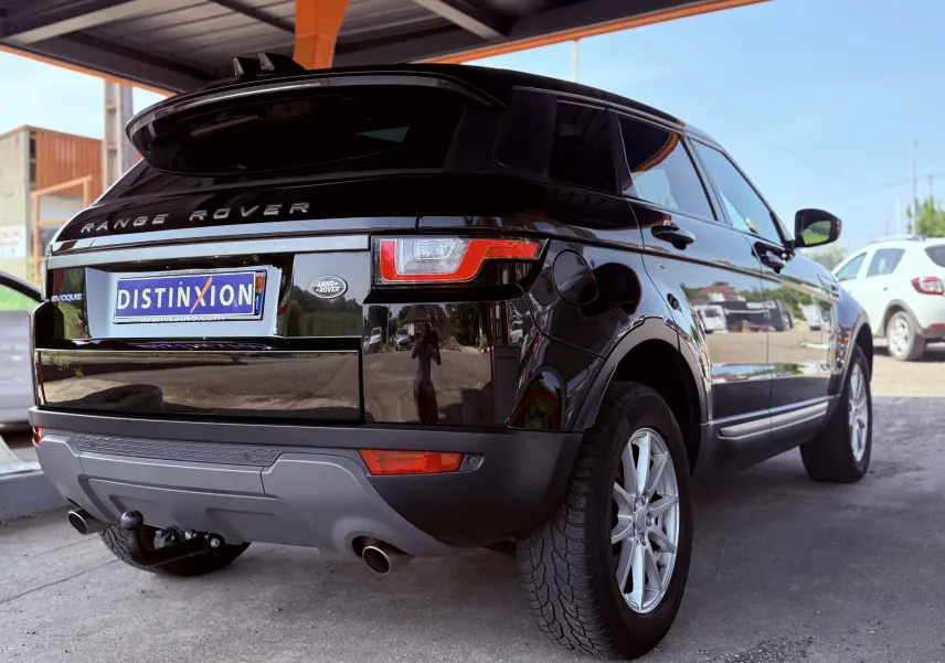 Vue 3/4 arrière droite d'un Range Rover Evoque noir brillant avec attelage et jantes argentées sous un abri.