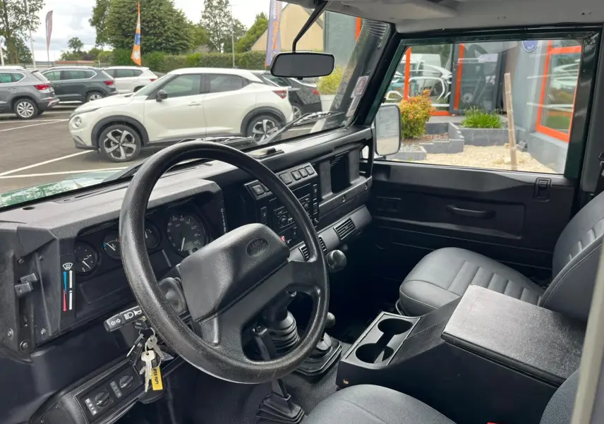 Intérieur du Land Rover Defender 90 vert de 2004, vue côté conducteur montrant le tableau de bord et la boîte manuelle.