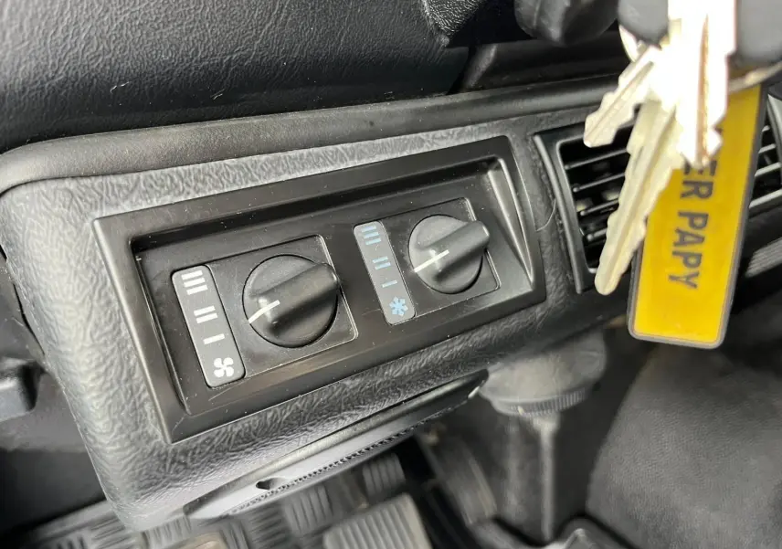 Gros plan sur les commandes de ventilation noires du tableau de bord du Land Rover Defender 90 vert de 2004.