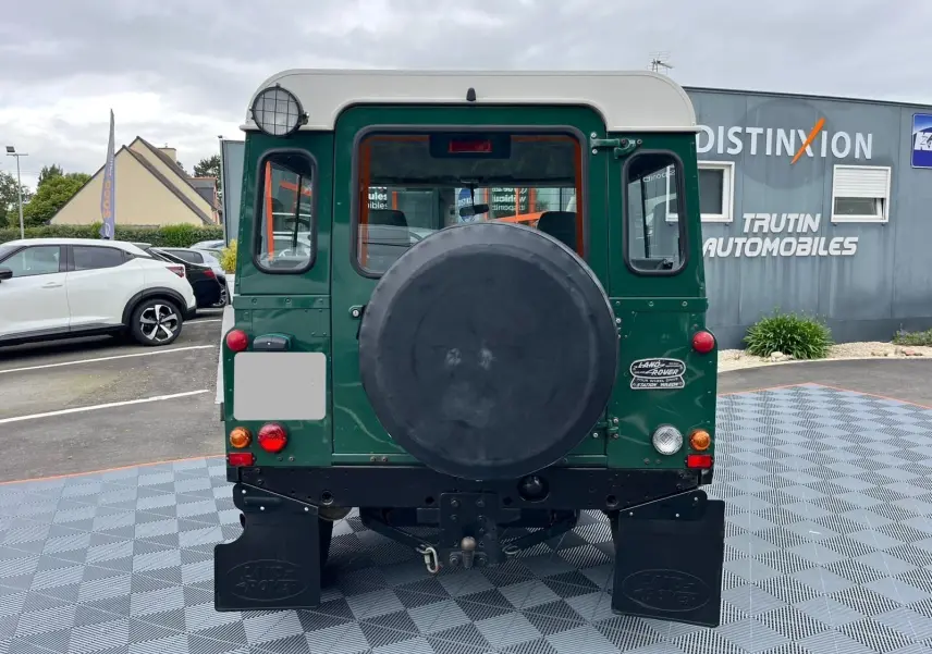 Vue arrière d'un Land Rover Defender 90 vert 2004 avec roue de secours et Hard Top blanc visible.