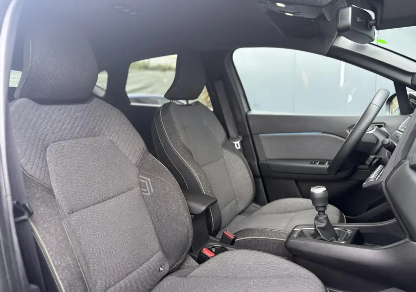 Vue intérieure côté droit du Renault Captur 2025, sièges tissu gris avec accoudoir central et levier de vitesses manuel.