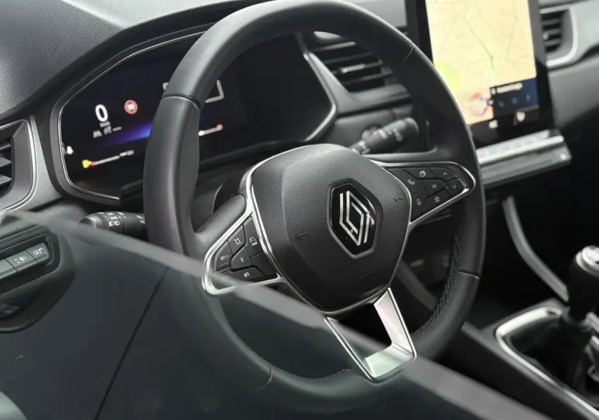 Vue rapprochée du volant noir et du tableau de bord numérique du Renault Captur 2025, avec écran tactile et levier de vitesse manuel.