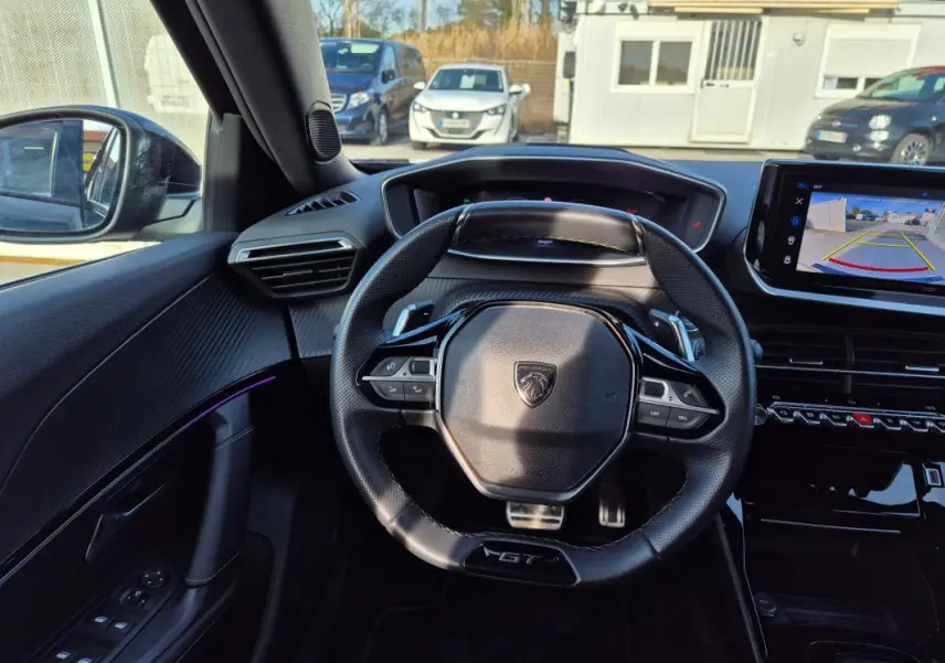 Vue intérieure centrée sur le volant noir GT du Peugeot 2008 Hybrid 145 avec écran tactile affichant la caméra de recul.