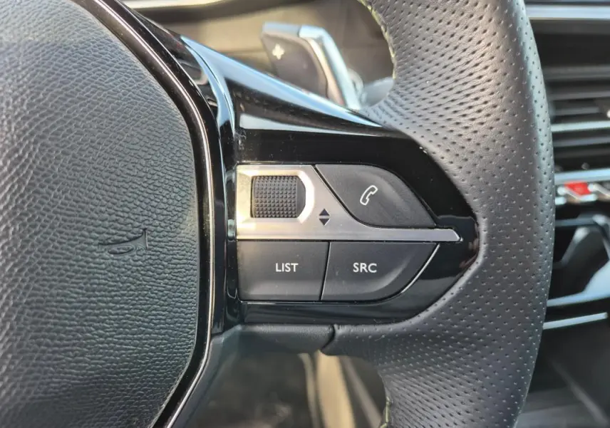 Gros plan sur la partie droite du volant noir perforé du Peugeot 2008 Hybrid 145 e-DCS6 GT 2024, avec commandes intégrées.