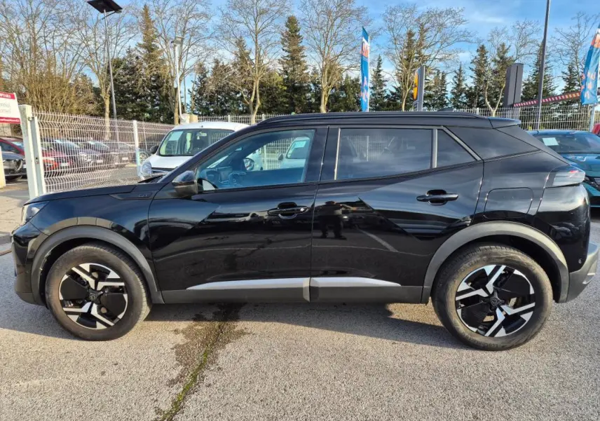 Vue de profil côté gauche d’un Peugeot 2008 Hybrid 145 e-DCS6 GT noir avec jantes alliage 18 pouces et barres de toit.