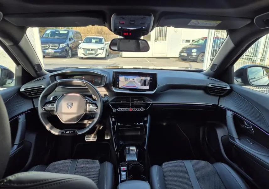 Vue intérieure avant du Peugeot 2008 Hybrid 145 e-DCS6 GT noir, avec tableau de bord numérique et écran tactile central affichant la caméra de recul.
