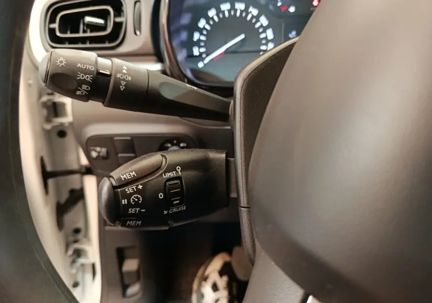 Gros plan sur la commande de régulateur de vitesse à gauche du volant dans l’habitacle d’une Citroën C3 blanche.