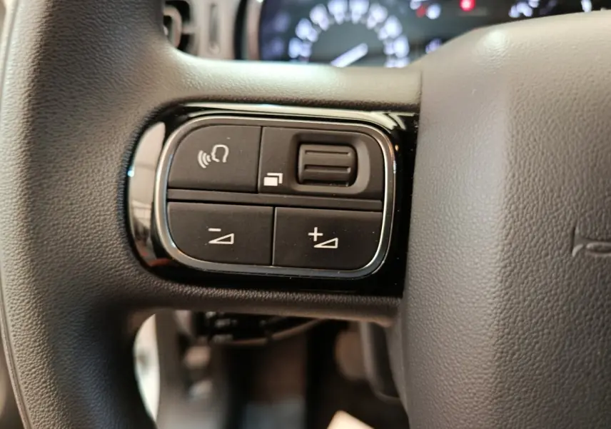 Gros plan sur les commandes multifonctions du volant noir d'une Citroën C3 blanche, version PureTech 83 2020.