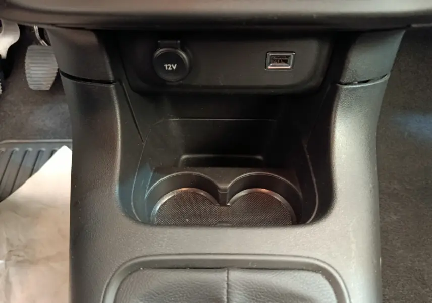 Gros plan sur la console centrale noire de la Citroën C3, montrant porte-gobelets, prise 12V et port USB.