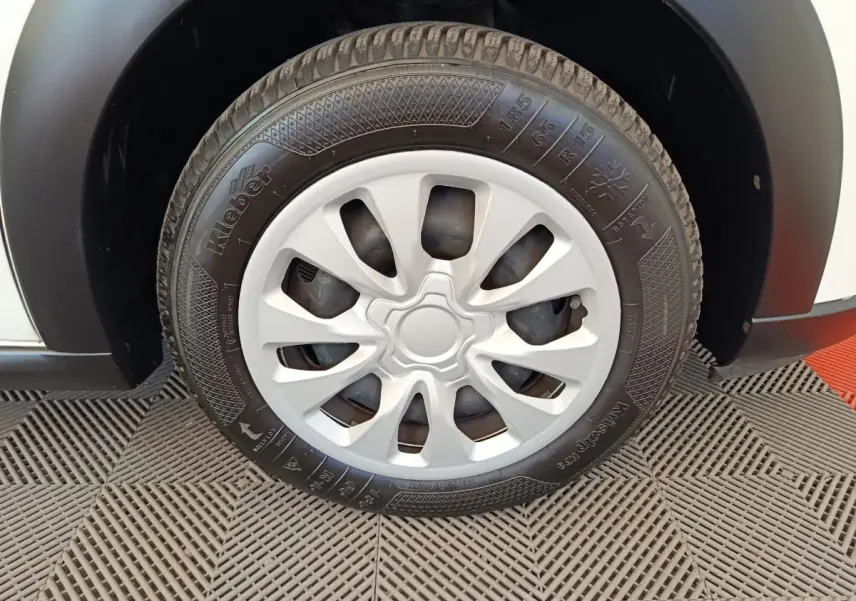 Gros plan sur la roue avant droite d'une Citroën C3 blanche, avec jante en plastique et pneu Kleber visible.