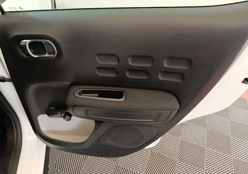 Vue intérieure de la porte avant gauche noire de la Citroën C3 blanche, mettant en valeur la poignée et le haut-parleur intégré.