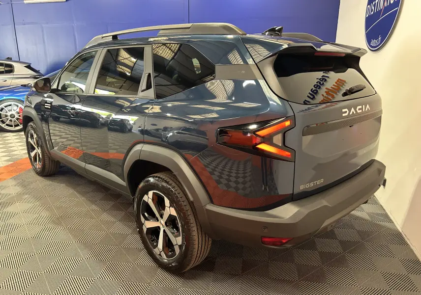 Vue 3/4 arrière droite du Dacia Bigster bleu indigo avec feux arrière en forme de flèche et hayon électrique.