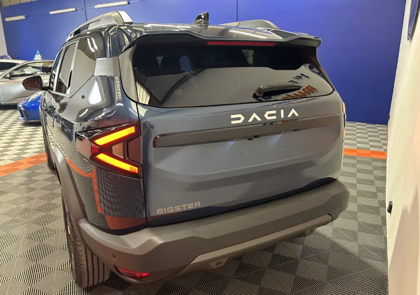Vue 3/4 arrière droite du Dacia Bigster bleu indigo avec feux arrière LED en forme de flèche et hayon électrique.
