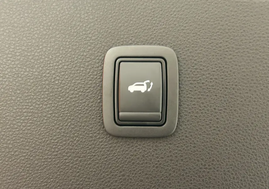 Bouton intérieur noir avec symbole blanc d'ouverture électrique du hayon sur fond de texture plastique grise.