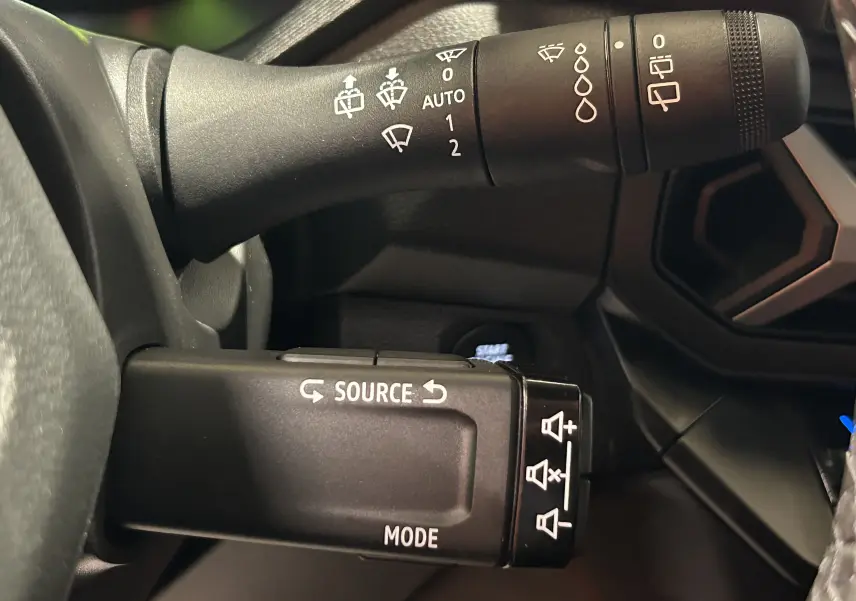 Gros plan sur les commandes au volant du Dacia Bigster 2026, avec leviers noirs et inscriptions blanches, intérieur sombre.