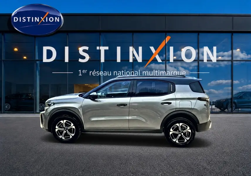 Profil droit d'un Citroën C3 Aircross gris mercury 2026 avec toit noir et jantes alu modernes, devant une vitrine Distinxion.