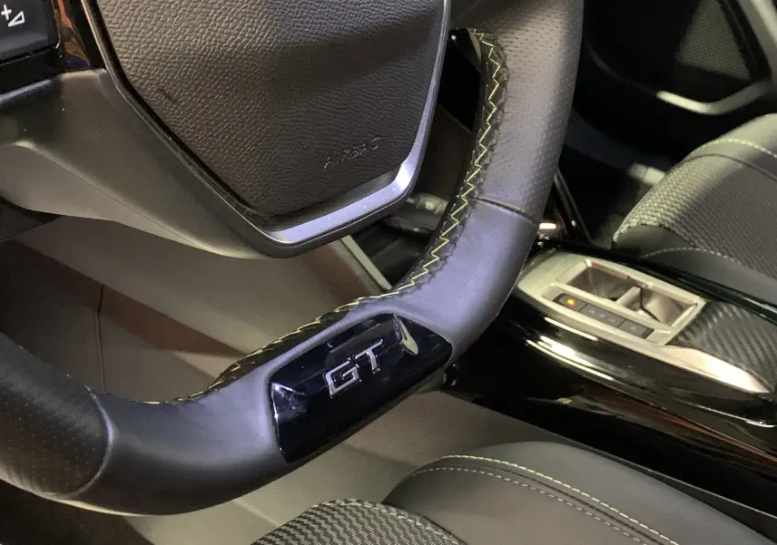 Gros plan sur le volant GT avec surpiqûres jaunes du Peugeot 2008 gris, intérieur cuir et détails carbone visibles.