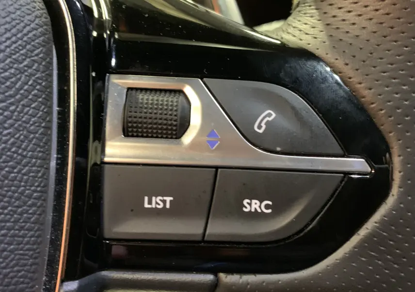 Gros plan sur les commandes du volant côté gauche du Peugeot 2008 gris, boutons pour appel et navigation audio.