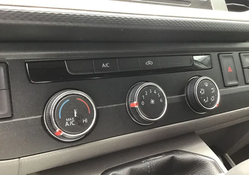Gros plan sur les commandes de climatisation du Volkswagen Transporter 6.1 blanc, avec boutons rotatifs et affichage clair.