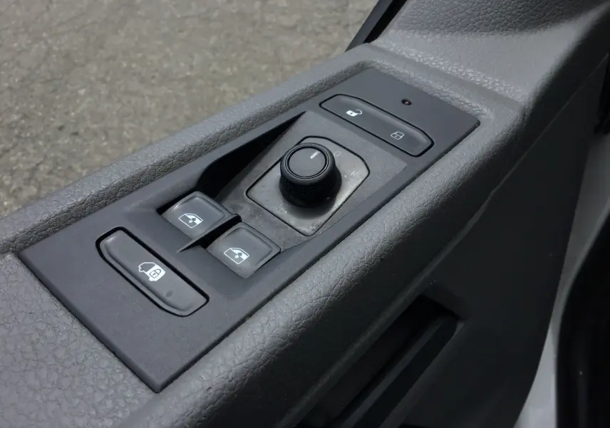 Gros plan sur les commandes de lève-vitres et réglage des rétroviseurs côté conducteur du Volkswagen Transporter 6.1 blanc.
