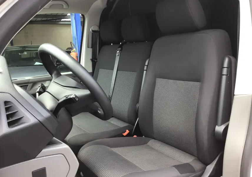 Vue intérieure côté conducteur du Volkswagen Transporter 6.1 Van blanc, montrant les sièges avant en tissu gris et noir.