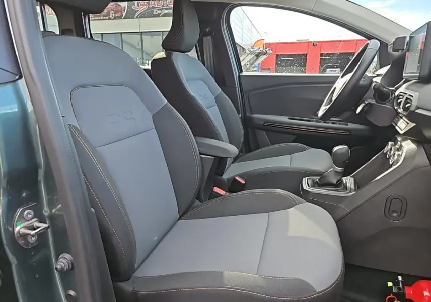 Vue intérieure côté conducteur du Dacia Jogger vert 2024, sièges avant gris avec surpiqûres contrastées et volant multifonctions.