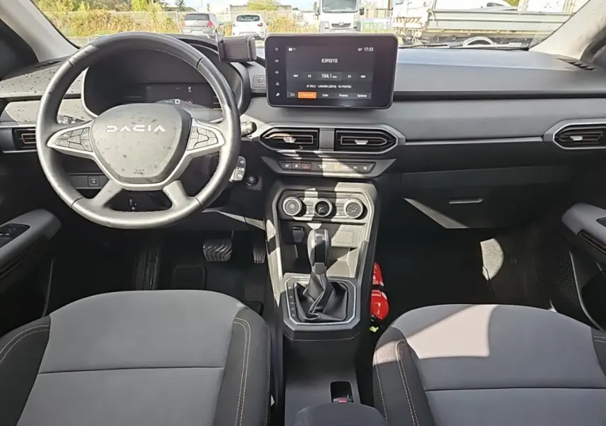 Vue intérieure avant du tableau de bord et volant DACIA Jogger avec écran tactile central et sièges gris.