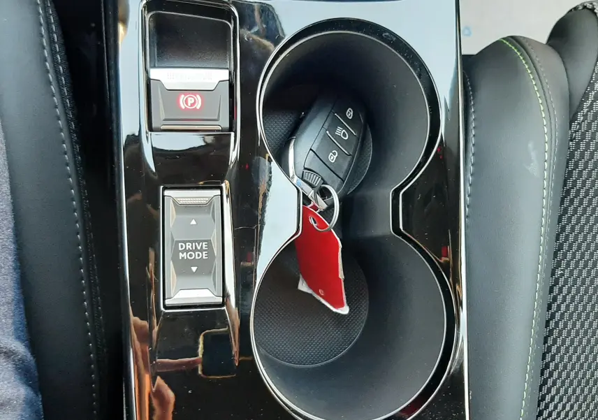 Vue plongeante sur la console centrale noire brillante d'une Peugeot 2008 gris selenium, avec clé dans porte-gobelet.