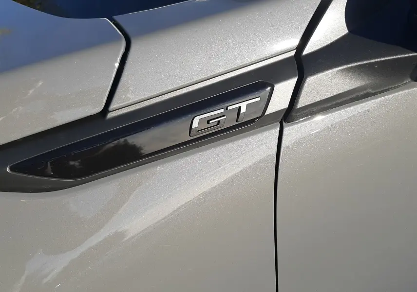 Gros plan sur l'emblème GT noir brillant sur la porte gris selenium côté gauche du Peugeot 2008 hybride 2025.