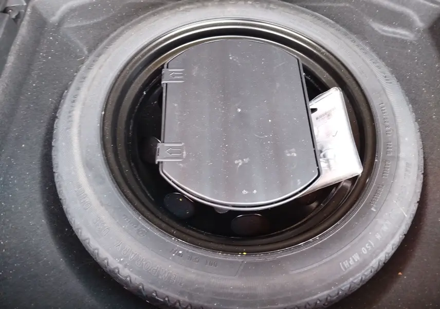 Vue plongeante sur la roue de secours noire et son kit de réparation dans le coffre du Peugeot 3008 Gris Platinium 2023.