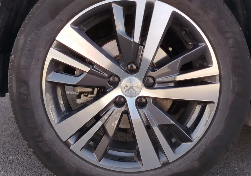 Gros plan sur la jante bi-ton noir et argent avec logo Peugeot au centre, montée sur un pneu Michelin.