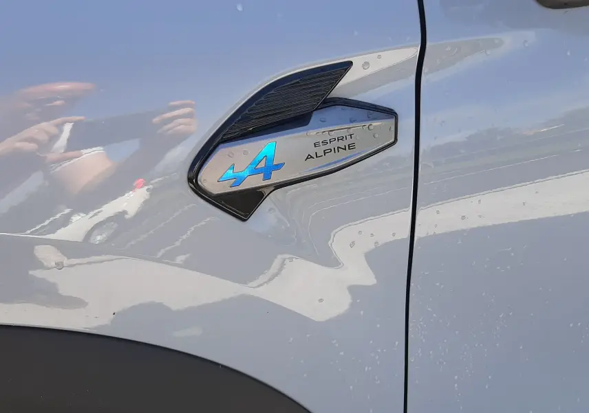 Gros plan sur l’écusson Esprit Alpine bleu sur la porte côté gauche d’une Renault Symbioz gris Rafale.