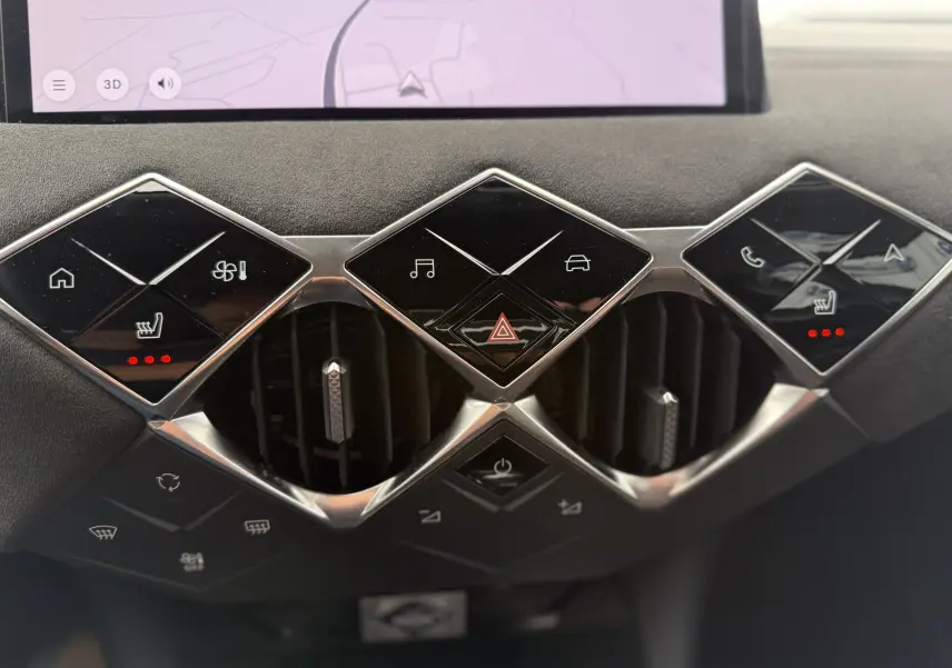 Gros plan sur la console centrale du DS3 hybride 2025, boutons noirs brillants en forme de losange avec éclairage rouge des sièges chauffants.
