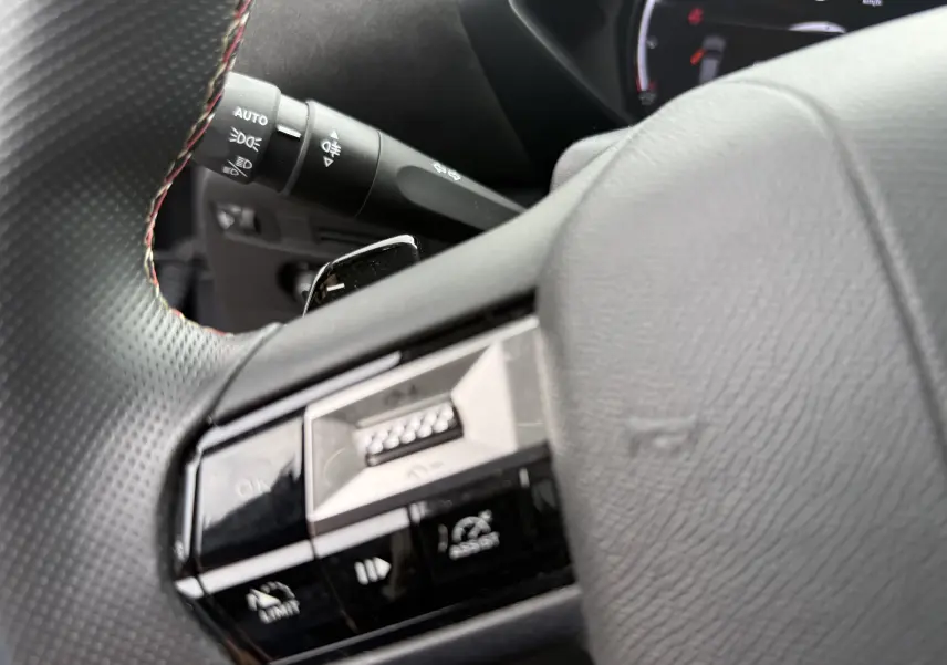 Gros plan sur la partie gauche du volant noir perforé du DS3 hybride 2025, avec commandes intégrées et levier de clignotant visible.
