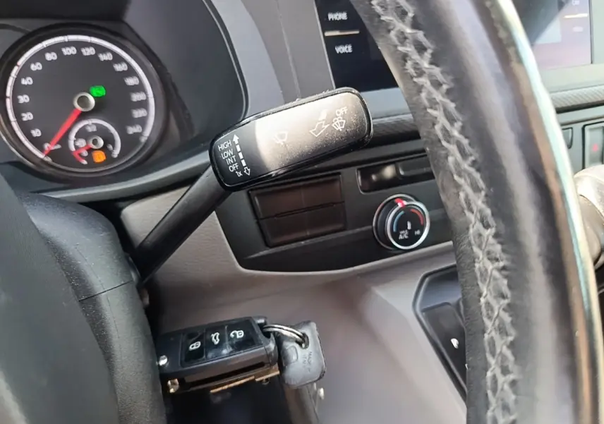 Gros plan sur le volant cuir et le commodo d’essuie-glace du Volkswagen Transporter gris foncé, tableau de bord partiel visible.